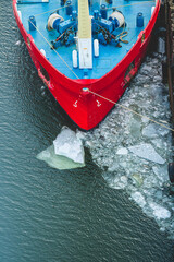 Fototapeta premium Red ship bow docked in icy harbor during cold winter evening.