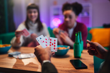 Fototapeta premium Diverse friends playing cards at a table with snacks and drinks, sharing laughter and bonding during a relaxed evening