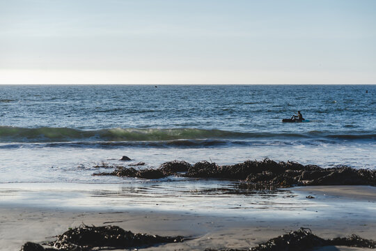 Kayakista en el oc&eacute;ano Pac&iacute;fico con rocas y huiro en primer plano, playa de Conc&oacute;n, Chile