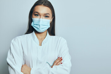 Health worker wearing a mask stands with arms crossed in a clinical setting during the day © verona_studio