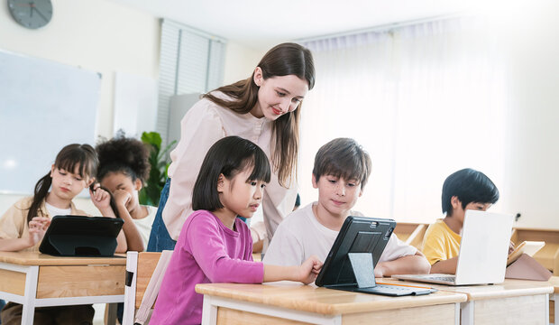 Portrait of smile teacher help elementary school children with digital tablets desks, show technology integration modern learning in classroom. Back to school, education.