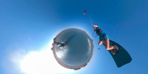 VR 360: Man does a selfie as female kiteboarder jumps past him on a sunny day. © helivideo