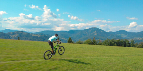 Fototapeta premium AERIAL Unrecognizable man speeds down a single trail on a green electric bicycle