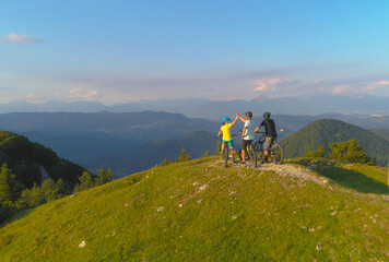 Obraz premium DRONE: Group of friends high fives after successful bike ride in green mountains