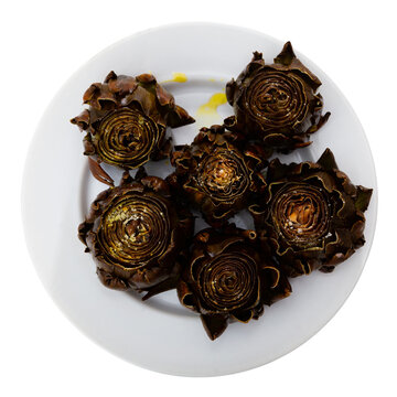 Crispy baked artichoke on a ceramic plate on a table with cutlery. Artichokes with spices for an appetizer. Isolated over white background