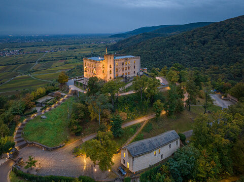 Aerial view of Hambach Castle atop a hill, illuminated against the dusk sky, overlooking vineyards and forests, Neustadt an der Weinstrasse, Rheinland-Pfalz, Germany.