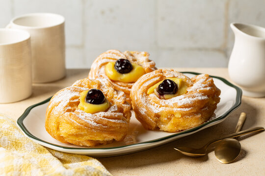 Table with Italian dessert Zeppole di San Giuseppe, zeppola - fried puffs made from choux pastry, filled and decorated with custard cream and cherry.