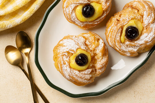 Top view of Italian dessert Zeppole di San Giuseppe, zeppola - fried puffs made from choux pastry, filled and decorated with custard cream and cherry.