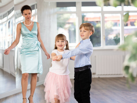 Boy and girl in pair train to dance vigorous hustle during classes. Children rehearse contemporary dancing movement. Female teacher conducts class for students