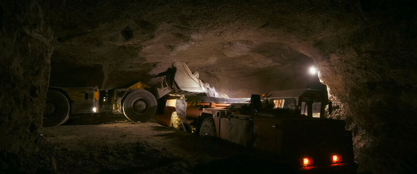 mining bulldozer pours gold ore into the body of a mine dump truck.