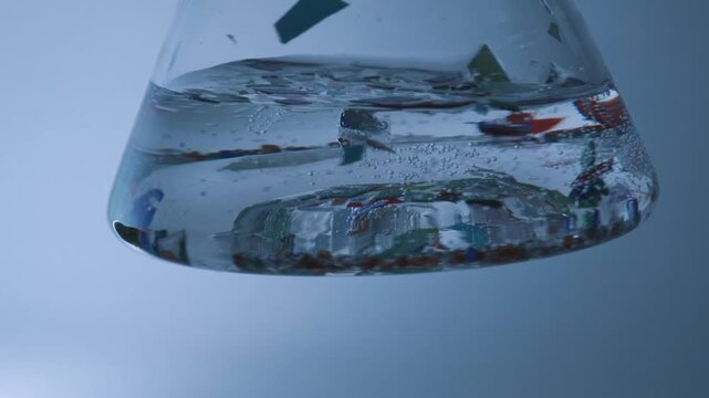 Colorful microplastic particles floating and sinking in a beaker of water showing contamination