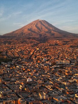 Aerial view of the majestic El Misti volcano looming over the dense urban sprawl, casting long shadows in the fading light, Arequipa, Arequipa, Peru.