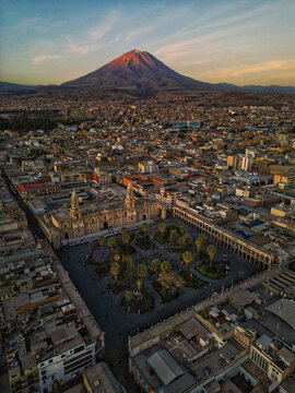 Aerial view of a sprawling cityscape nestled beneath the majestic, sun-kissed El Misti volcano, showcasing the Plaza de Armas and colonial architecture, Arequipa, Arequipa, Peru.