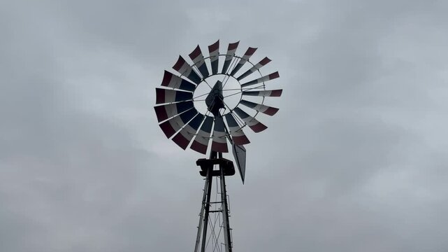 Close up of a windmill weather vane with red white and blue blades spinning against an overcast sky
