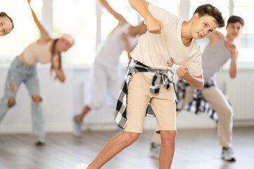 Fototapeta premium Dynamic teenage boy training hip hop slides in dancehall during workout session in group