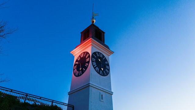 Aerial view of the iconic clock tower bathed in the soft glow of twilight, its face a stark contrast against the deep blue sky, Petrovaradin, Vojvodina, Serbia.