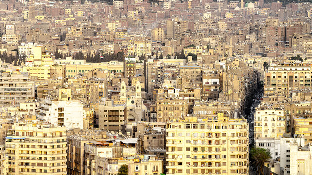 View of sun-drenched buildings and structures creating a dense urban tapestry under a hazy sky, a blend of old and new architecture, Cairo, Cairo Governorate, Egypt.