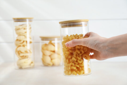 Woman with different types of pasta at beige table, closeup