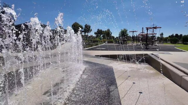Water jets in a splash park, with dynamic fountain streams and a playground in the background. Family friendly recreational water play area in suburban neighborhood. Manor Lakes, Melbourne, Australia