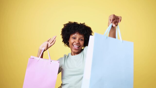 Happy shopper holding shopping bags on yellow background