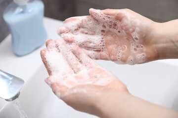 Fototapeta premium Woman washing hands with soap above white sink indoors, closeup