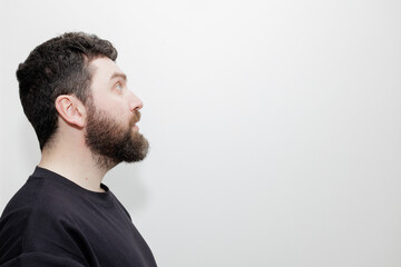 Obraz premium A minimalist portrait of a bearded man wearing a black sweatshirt, looking away against a neutral white background. Stock photo