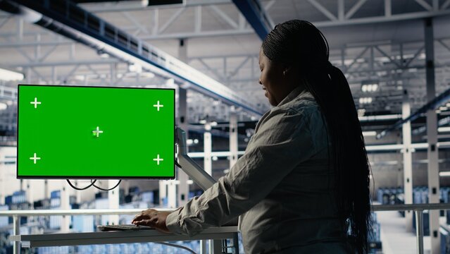 Software developer in server hub using chroma key workstation to scan equipment for issues. African american woman in data center uses isolated screen PC to do backups, camera B