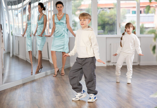 Artistic tween boy joyfully mimicking classic comedic stroll of Charlie Chaplin during dance rehearsal overseen by female teacher in choreographic studio..