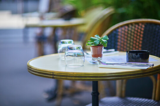 Empty outdoor cafe table on a quiet Paris street with upside-down glasses, cutlery, an ashtray, and a small potted succulent.
