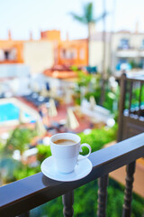 Fototapeta premium Cup of coffee on a hotel balcony overlooking a swimming pool and tropical courtyard in Tenerife, Canary Islands, Spain.