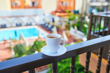 Fototapeta premium Cup of coffee on a hotel balcony overlooking a swimming pool and tropical courtyard in Tenerife, Canary Islands, Spain.