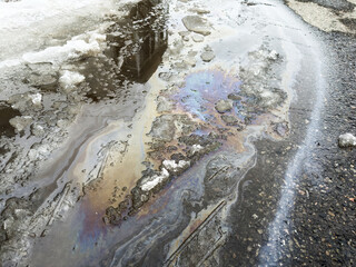 Fototapeta premium La surface de la rue est recouverte d'une fine couche de pétrole et de glace. Gros plan sur une nappe de pétrole répandue au sol.