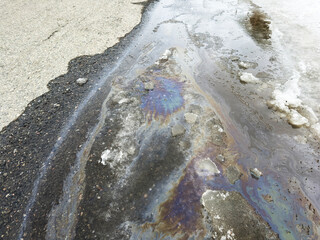 Fototapeta premium La surface de l'eau est recouverte d'une fine couche de pétrole et de glace. Gros plan sur une nappe de pétrole répandue au sol.