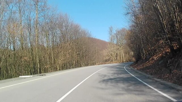 Dry wintertime road ride video on mountain pass Pezinska Baba, western Slovakia, during sunny winter day of february 2026. Naked trees, road signs and abandoned building visible along the road