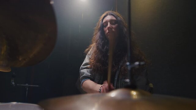 Woman drummer plays a drum kit, drumstick. Female musician beats a rock rhythm on drums, cymbals. Girl artist is rehearsing in a room or performing on festival stage. Alternative indie band in club