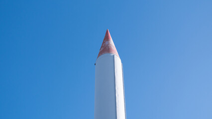 Naklejka premium Tall White Pencil Tip Pointing Skyward Against Clear Blue Backdrop, Minimal Composition Conveying Creativity And Focus, Bright Daylight Highlighting Sharp Lead And Vertical Geometry