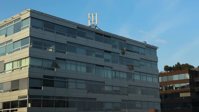 Two Rope Access Technicians Abseiling on Glass Office Building Facade