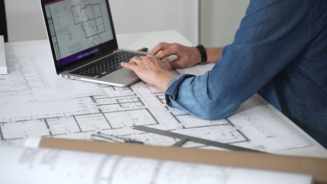 Architect drawing and measuring blueprints on a desk, creating detailed floor plans and designs for construction projects, demonstrating precision and expertise in architectural planning