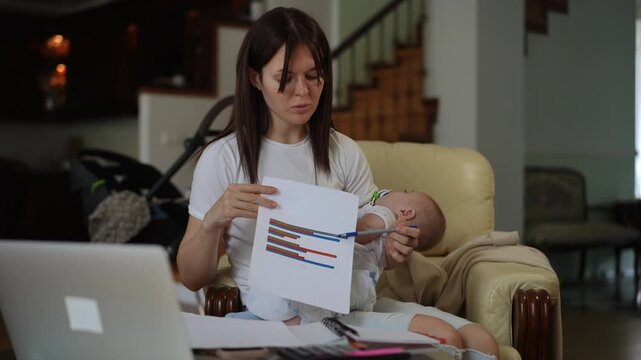 Busy businesswoman working remotely from home, holding her sleeping baby while presenting a business chart during an online video conference