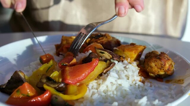 Woman eating rice with grilled vegetables and chicken using knife and fork casual meal healthy lifestyle indoor dining concept