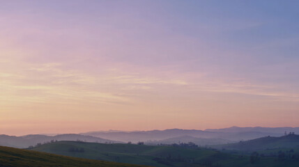 Fototapeta premium Light pastel dawn sky over rolling hills with subtle cross silhouette at distance, calm gradient colors, peaceful and uplifting easter morning mood, wide cinematic composition. with copy space