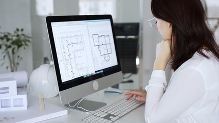 Woman architect analyzing construction blueprint on computer screen in modern design office, planning new building project. Business and architecture concept © rogerphoto