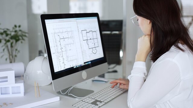 Woman architect analyzing construction blueprint on computer screen in modern design office, planning new building project. Business and architecture concept