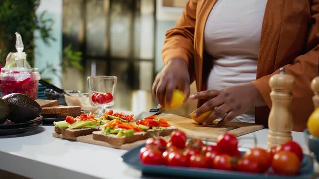 African american woman squeezing lemon juice on avocado on toast recipe, recording meal prep and dish development for online video. Content creator presenting rich in proteins healthy breakfast idea.