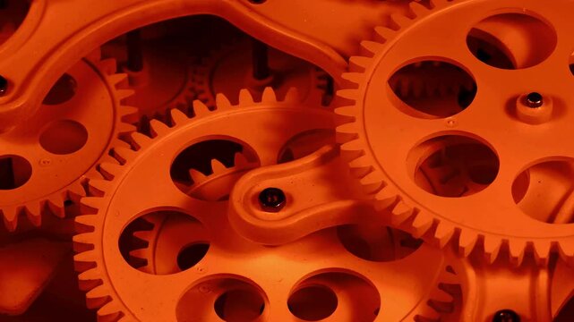 Close-up of interlocking gears illuminated with warm orange light, symbolizing energy, heat, power and industrial motion.