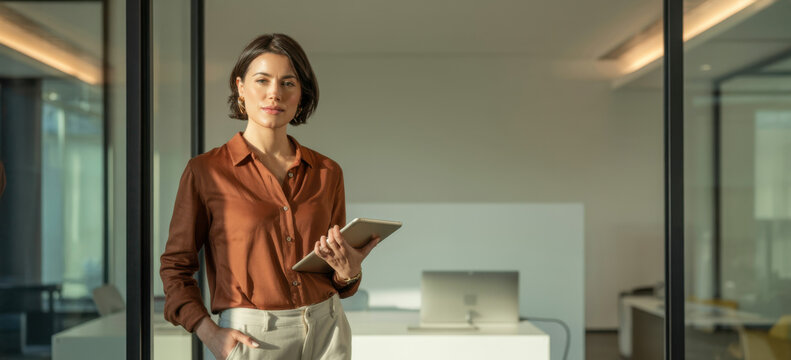 Portrait of young Hispanic professional business woman standing in office. Happy female company executive, smiling businesswoman entrepreneur corporate leader manager looking at camera using tablet.