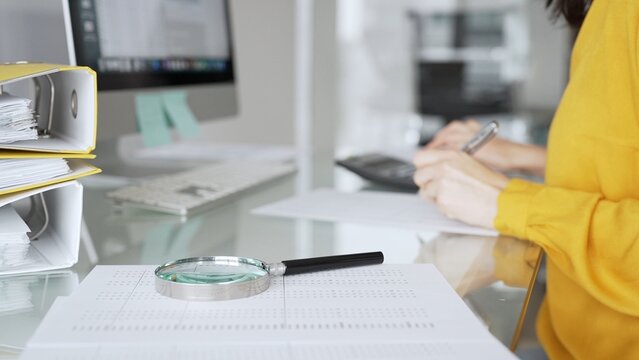A woman in a yellow blouse performs financial calculations and reviews paperwork as part of a business tax audit in her office. Finance analysis and tax compliance