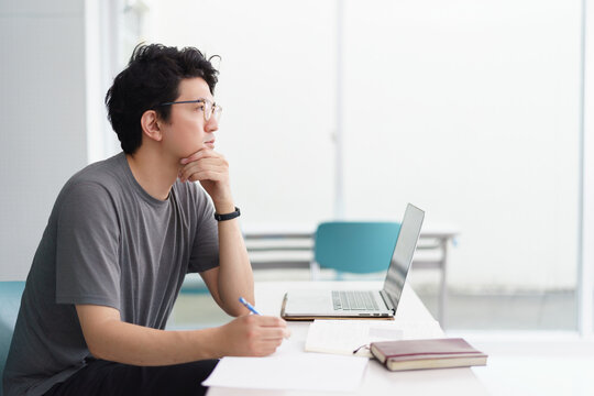 大学でパソコンや筆記用具を持ちカジュアルな服装で前方を真剣な表情で見る男性