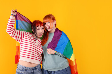 Lovely lesbian couple with rainbow flag on yellow background, space for text. LGBT concept