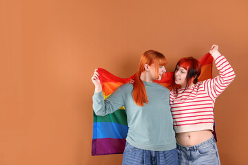 Lovely lesbian couple with rainbow flag on brown background, space for text. LGBT concept